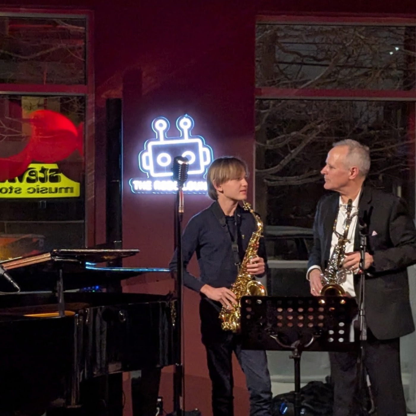 Two saxophonists performing beside the piano.